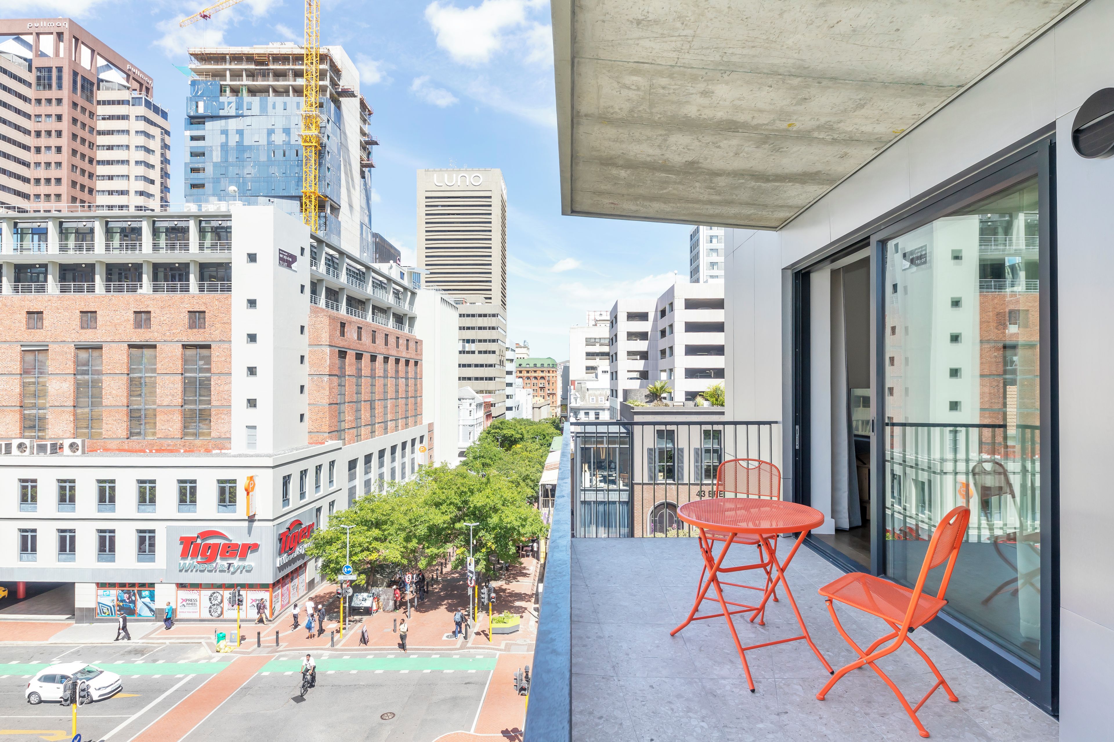 A balcony with orange chairs, overlooking a city street with buildings, including a 'Tiger' restaurant, and a 'Luno' building.