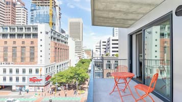 A balcony with orange chairs, overlooking a city street with buildings, including a 'Tiger' restaurant, and a 'Luno' building.