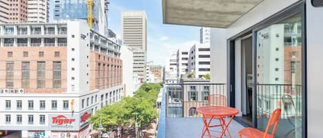 A balcony with orange chairs, overlooking a city street with buildings, including a 'Tiger' restaurant, and a 'Luno' building.