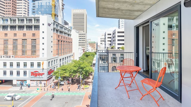 A balcony with orange chairs, overlooking a city street with buildings, including a 'Tiger' restaurant, and a 'Luno' building. - The Barracks (Cape Town)