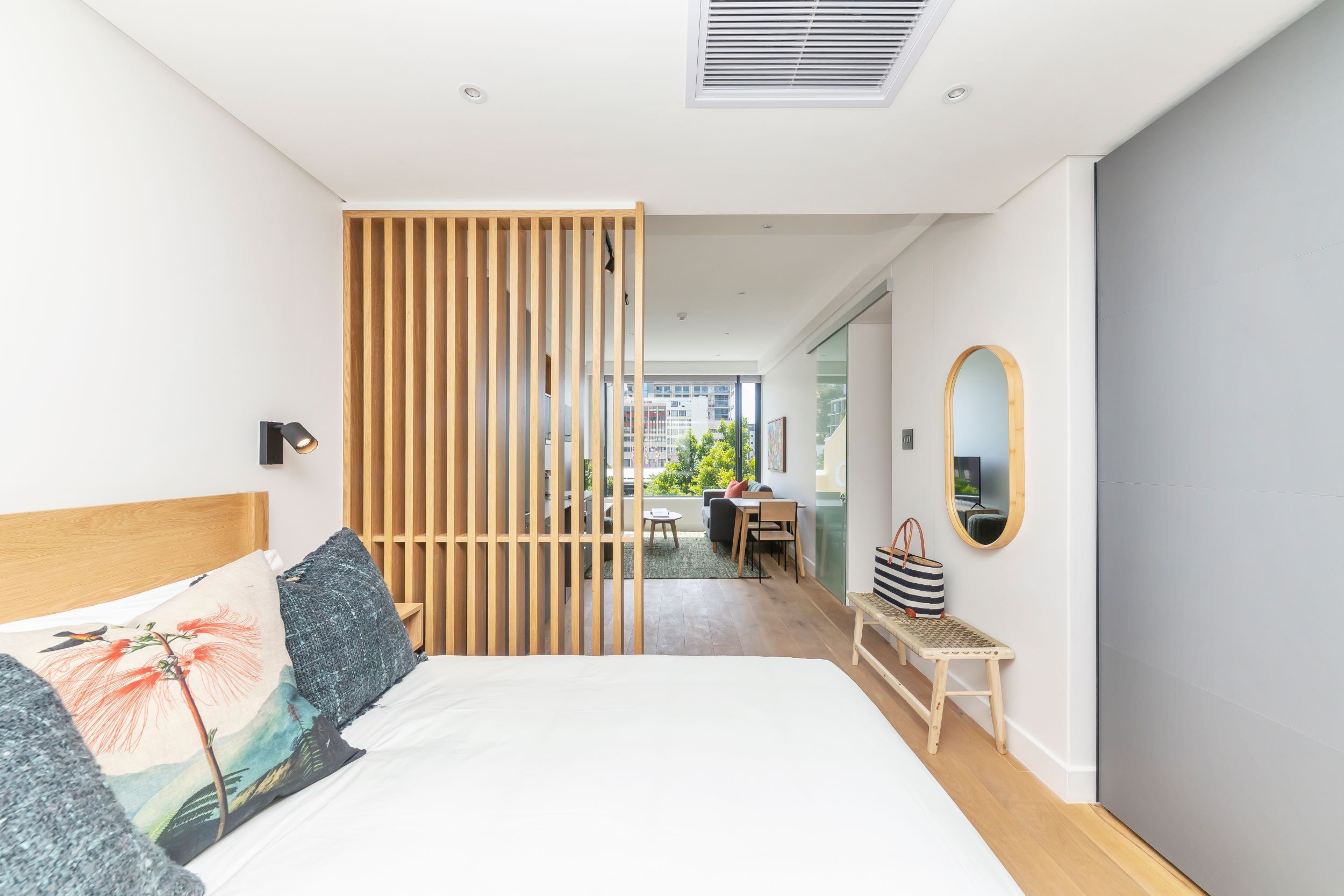 A modern bedroom with a large bed, a wooden partition, a desk, and a view of the outside.