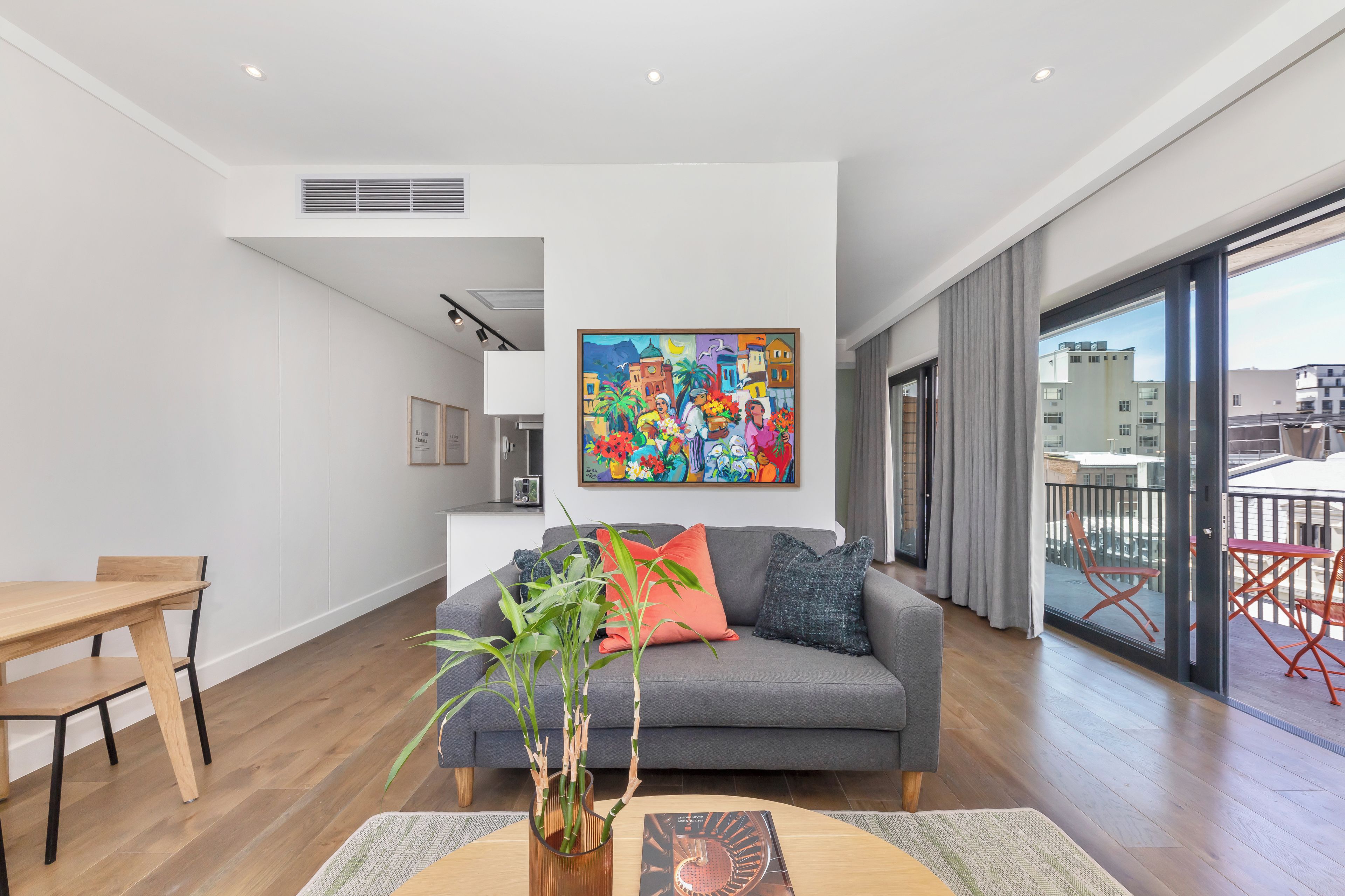 A modern living room with a grey sofa, wooden dining table, and a large window with a city view.