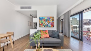 A modern living room with a grey sofa, wooden dining table, and a large window with a city view. - The Barracks (Cape Town)