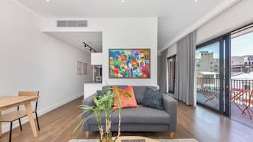 A modern living room with a grey sofa, wooden dining table, and a large window with a city view.
