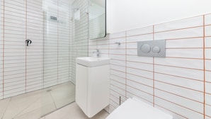 A modern bathroom with a glass shower enclosure, a white sink, and a mirror. - The Barracks (Cape Town)
