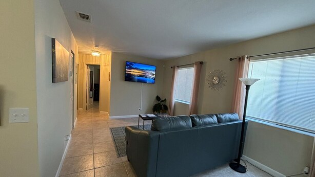 Una sala de estar con sofá, televisor, reloj y ventana con persianas.