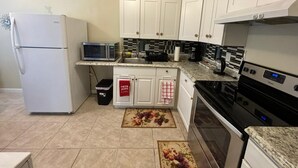 Una cocina con gabinetes blancos, un refrigerador, un microondas, una estufa y un lavaplatos.