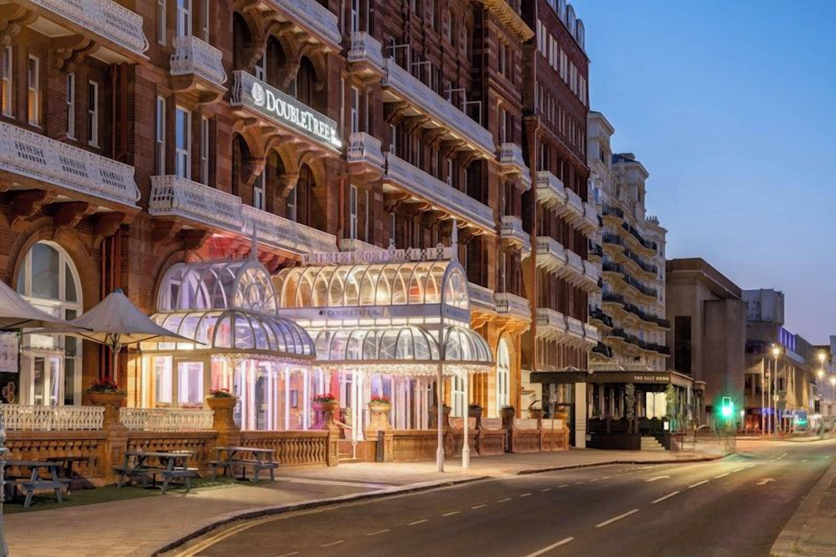 Ein Hotel mit einer klassischen Fassade, mehreren Balkonen und einer markanten Glasarchitektur am Eingang.