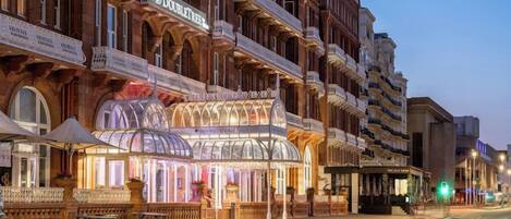 Ein Hotel mit einer klassischen Fassade, mehreren Balkonen und einer markanten Glasarchitektur am Eingang.