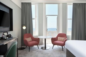 Habitación de hotel con cama, dos sillones, una mesa redonda, televisor y vista al mar.