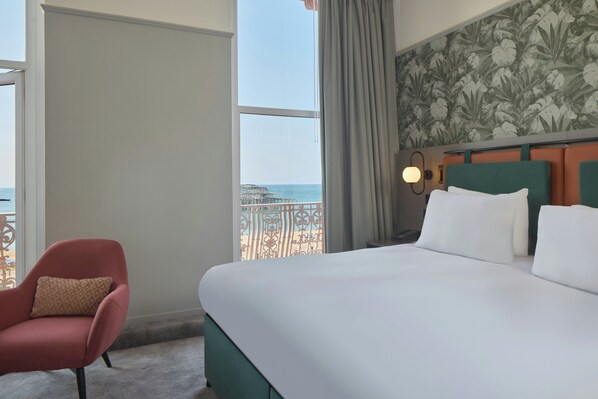 A hotel room with a large bed, a chair, a view of the beach, and a balcony with a railing. - Doubletree By Hilton Brighton Metropole (Brighton)