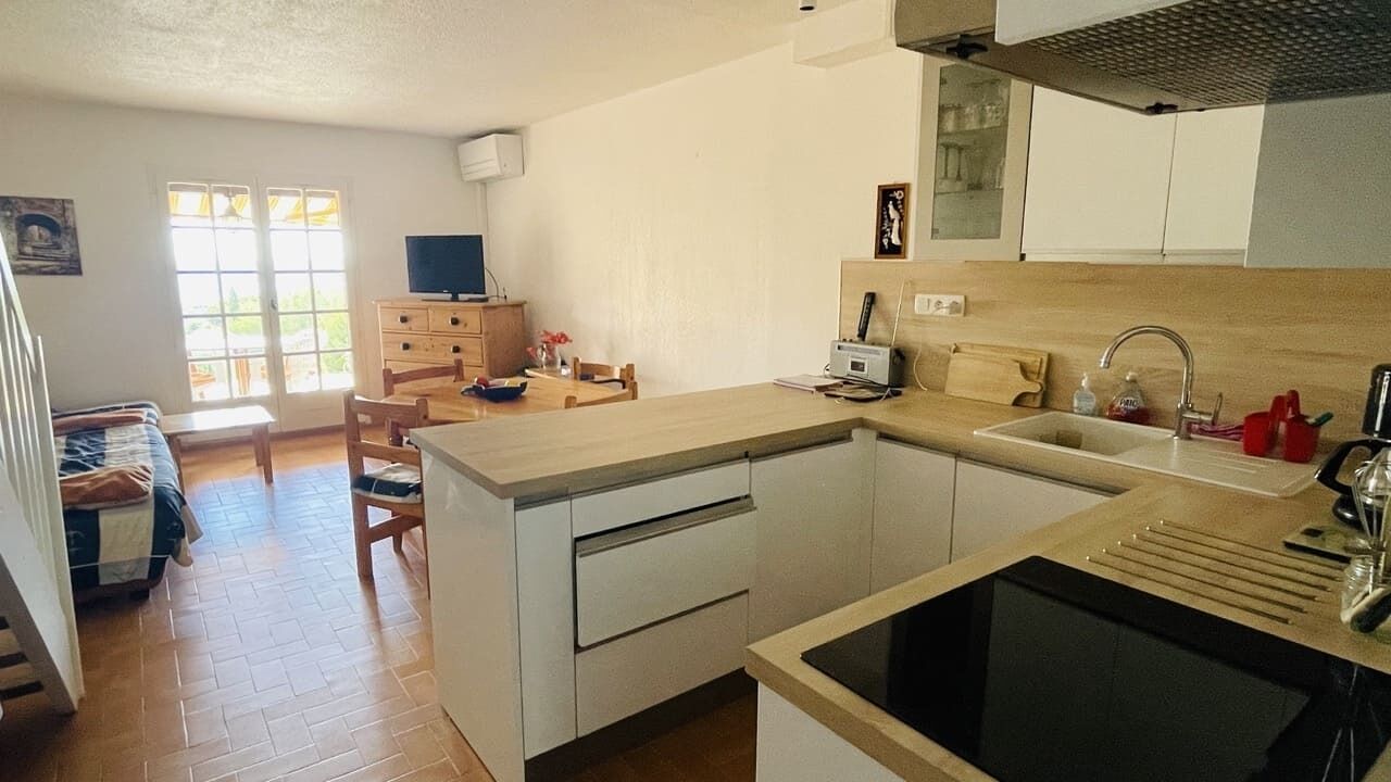 A compact kitchen with a sink, stove, and wooden cabinets. There is a dining area with a table and chairs.