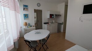 A compact kitchen with white cabinets, a sink, and a small countertop. There is a dining table with two chairs in the center of the room. - Cozy 24 m² studio near the sea (La Tranche-sur-Mer)