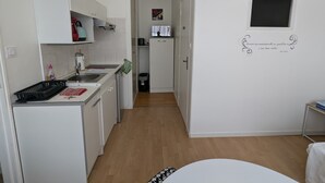 A compact kitchen with white cabinets, a sink, and a small refrigerator. A TV is mounted on the wall, and there's a decorative quote. - Cozy 24 m² studio near the sea (La Tranche-sur-Mer)