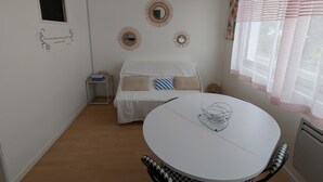 A small, well-lit room with a bed, a round table, and a window with sheer curtains. - Cozy 24 m² studio near the sea (La Tranche-sur-Mer)