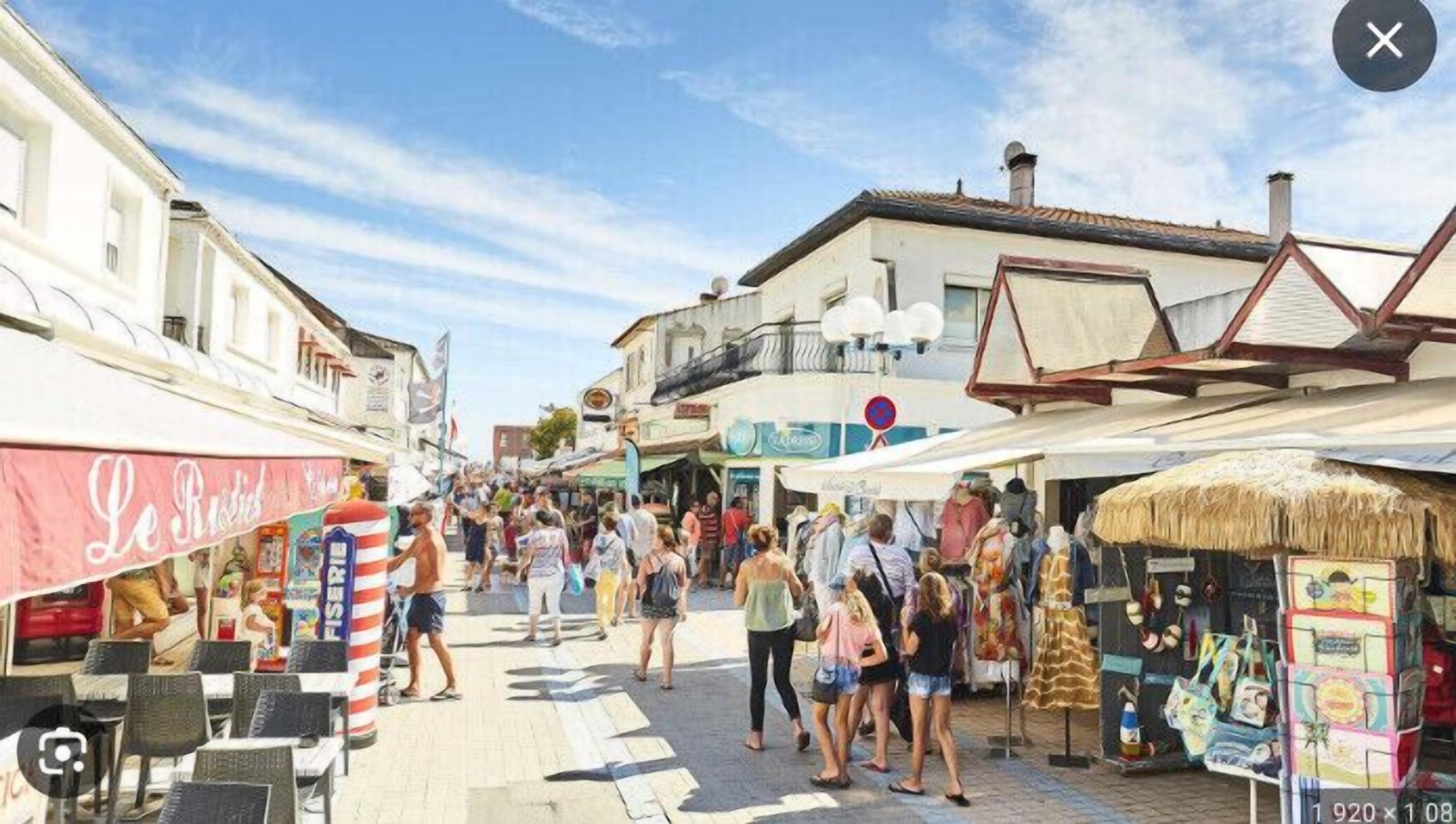 A bustling street with shops and cafes, a pedestrian crossing, and a clear sky.
