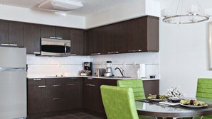 Una cocina moderna con armarios de madera oscura, electrodomésticos de acero inoxidable y una mesa redonda de vidrio con sillas verdes.