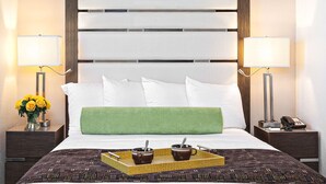 Habitación de hotel con una cama grande, dos mesitas de noche con lámparas, un cojín verde y una bandeja con dos tazas.