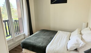 Relax in this serene bedroom with a large window and balcony view, featuring a comfortable bed and artwork above.