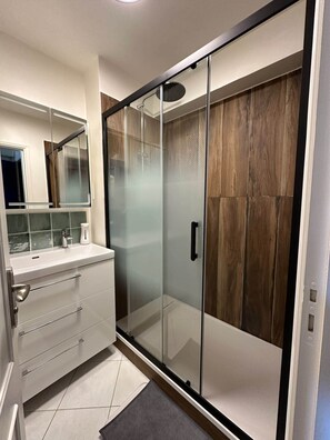 Experience a sleek bathroom with a glass-enclosed shower, vanity, and tile floor.