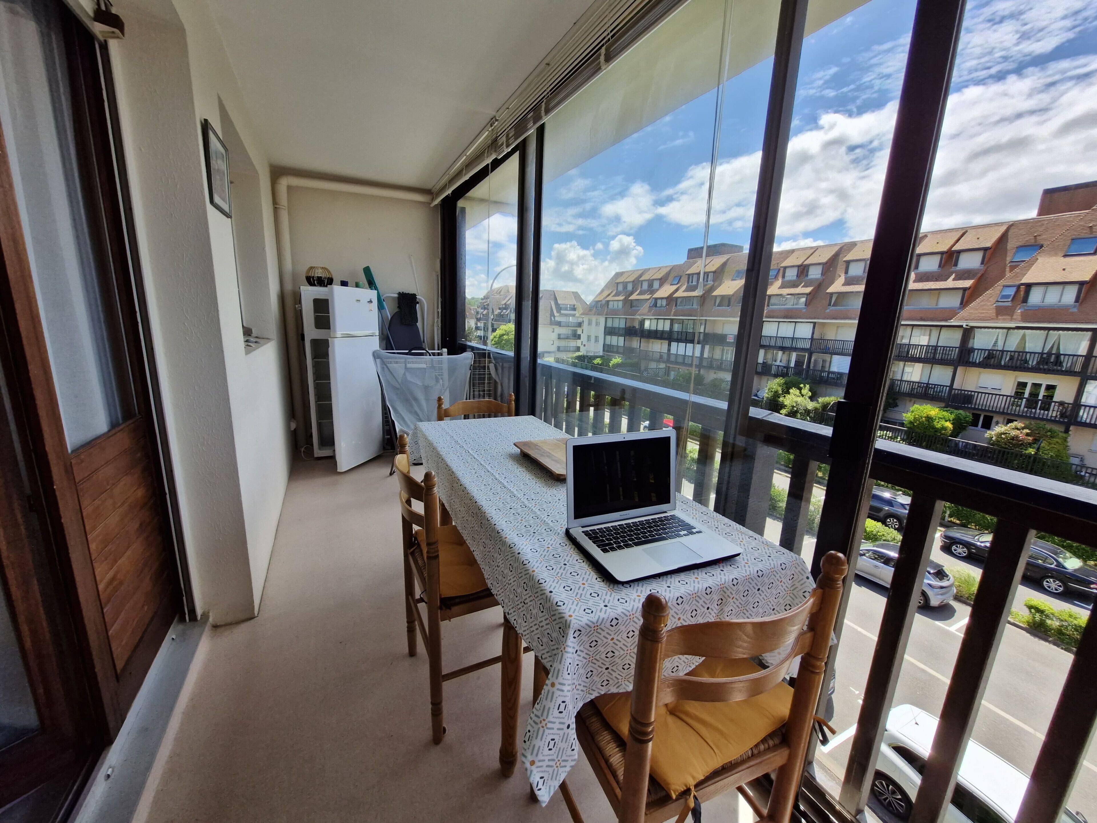 Un balcone con tavolo, sedie, un portatile e un frigorifero.