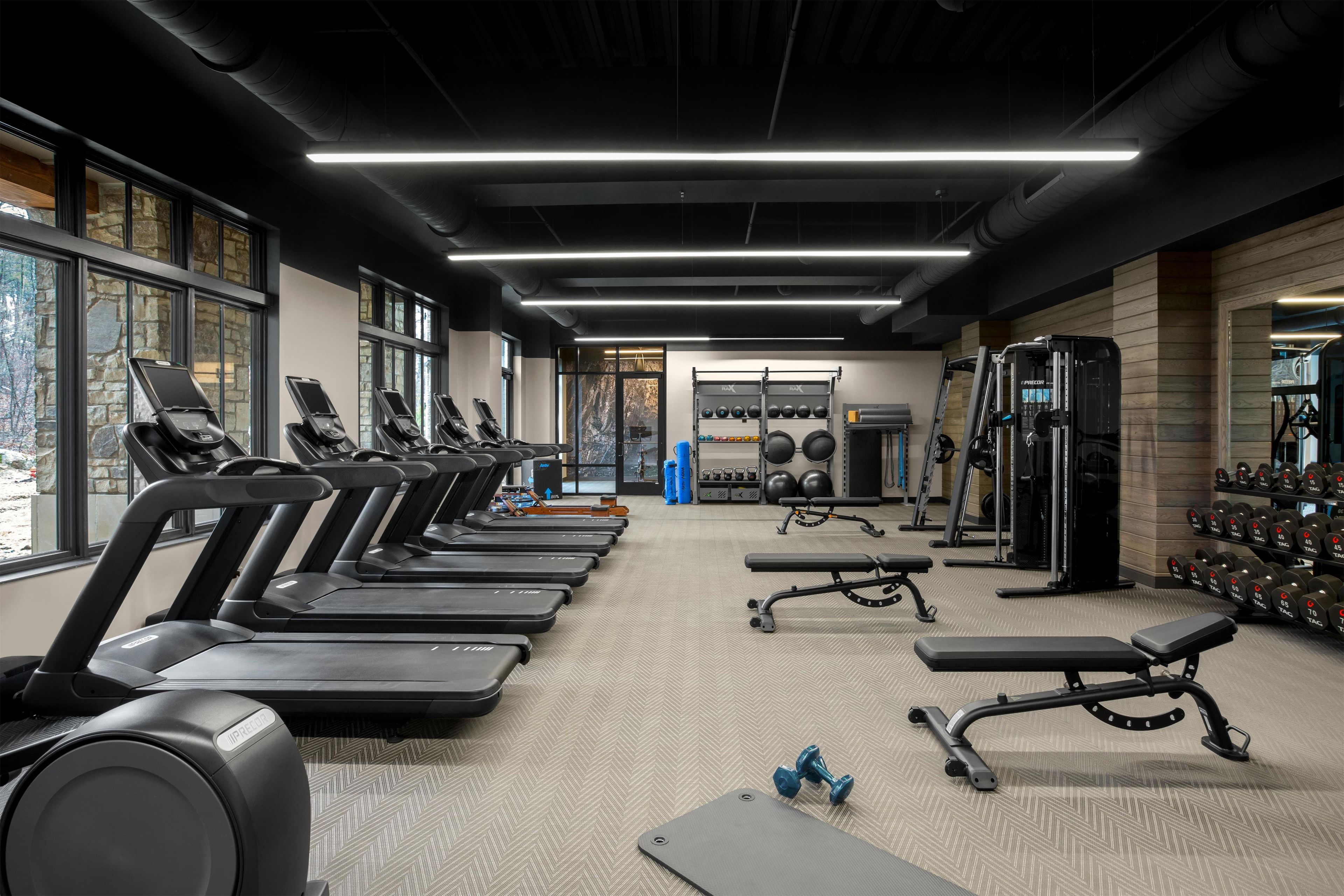 Un gimnasio con cintas de correr, bancos de pesas y pesas sueltas.