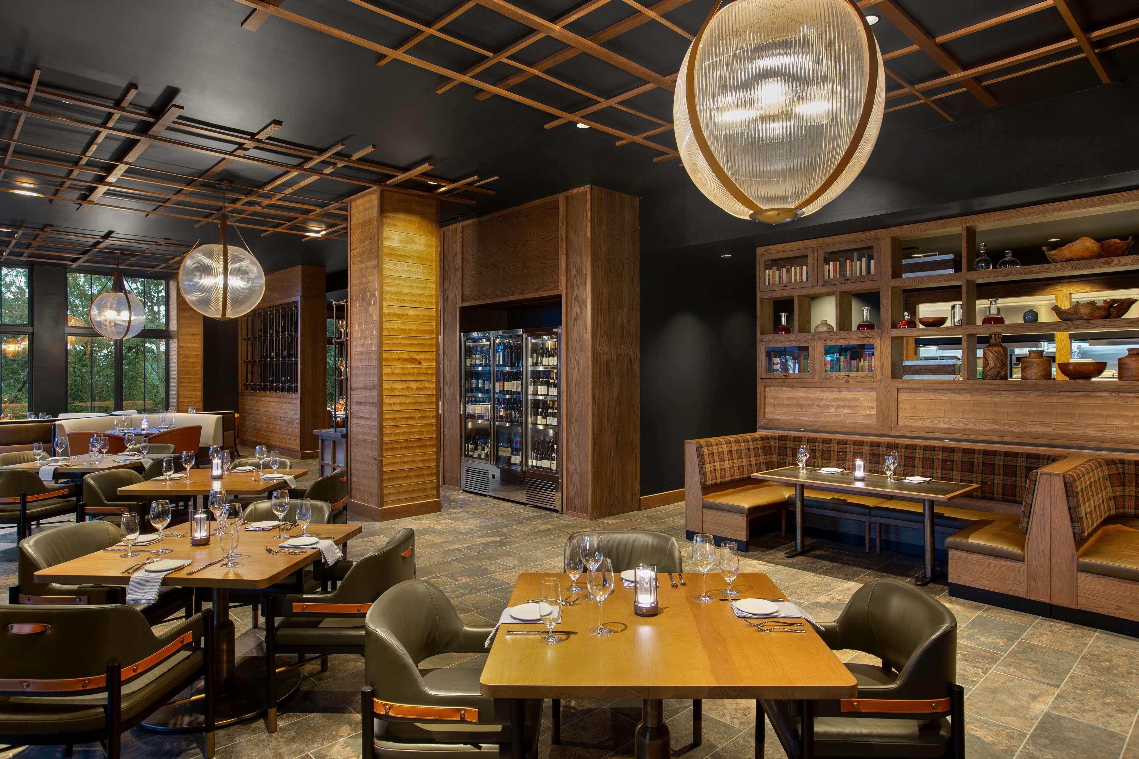 A restaurant with wooden tables and chairs, a bar area, and a wine display.