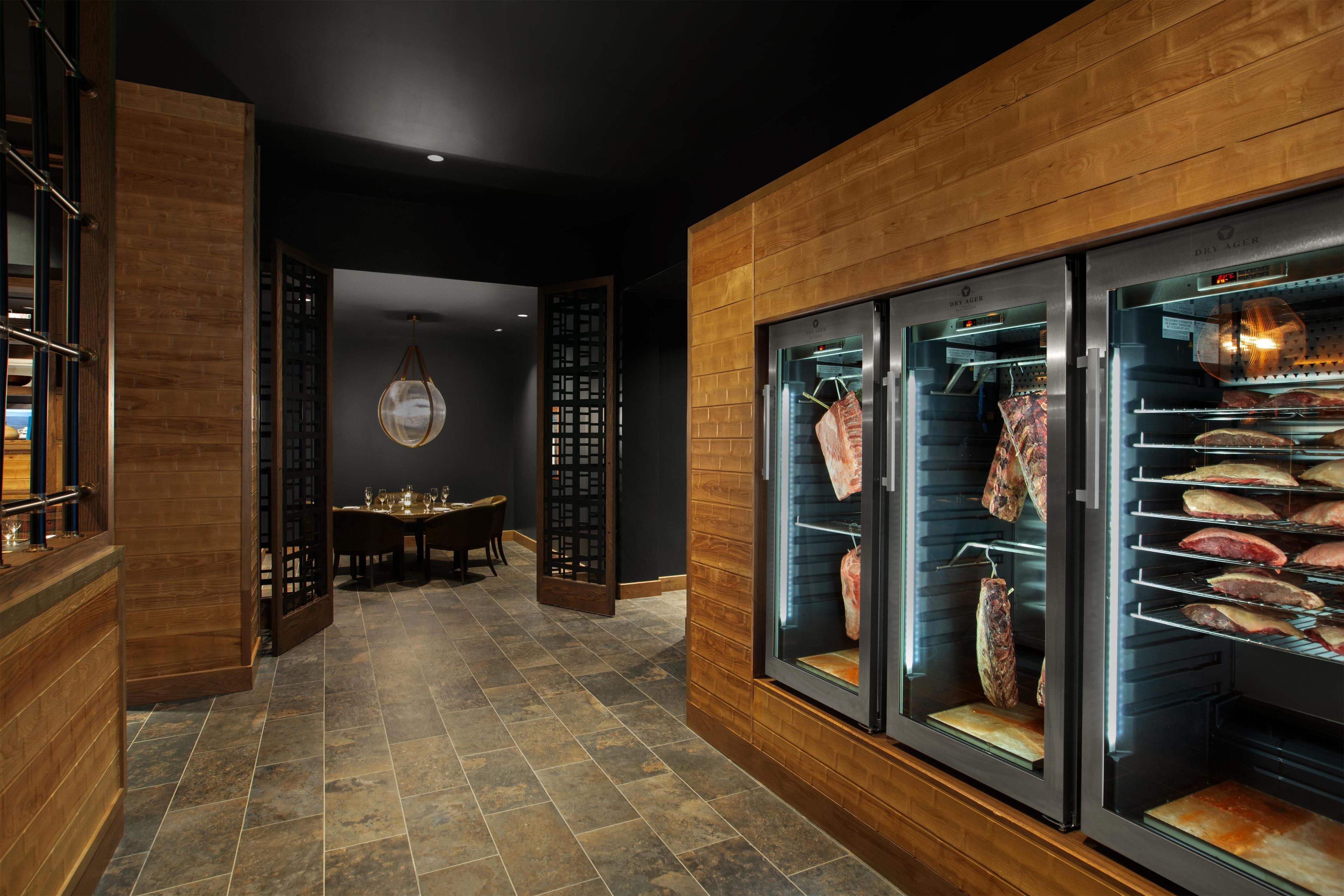 A restaurant interior with a dining area, a wall-mounted meat display, and a modern ceiling design.