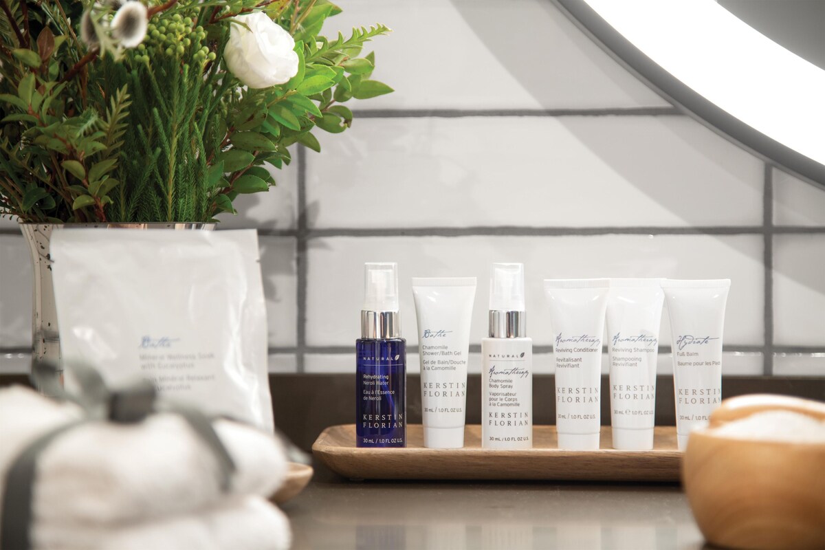 Un meuble-vasque de salle de bain avec des produits de soins pour la peau, un vase blanc orné de feuillage vert et une fleur blanche.