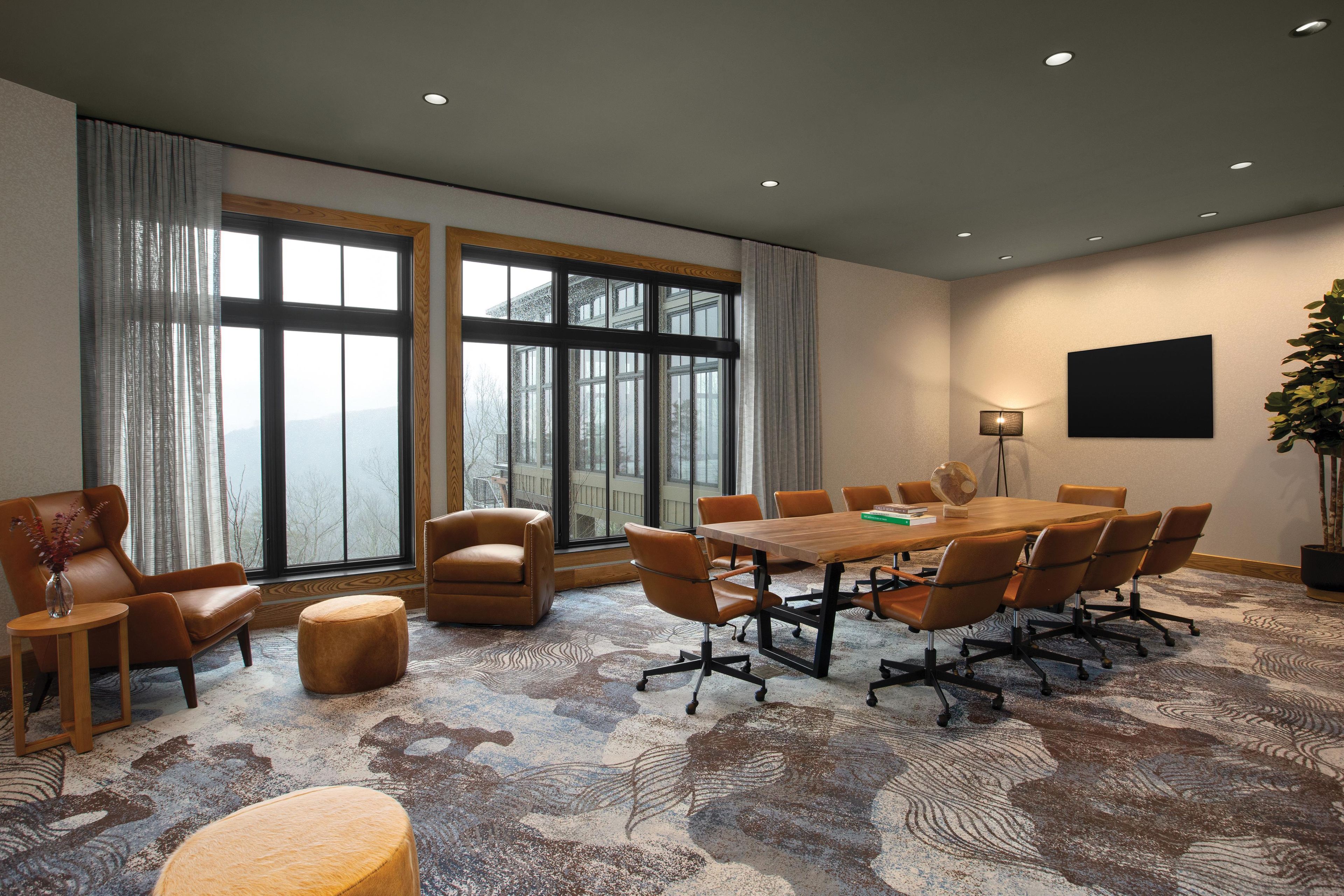 A conference room with a large table, multiple chairs, a potted plant, and a view through large windows.