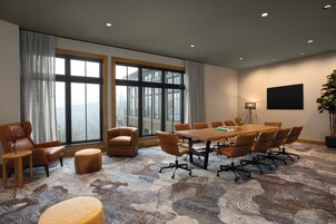 A conference room with a large table, multiple chairs, a potted plant, and a view through large windows.