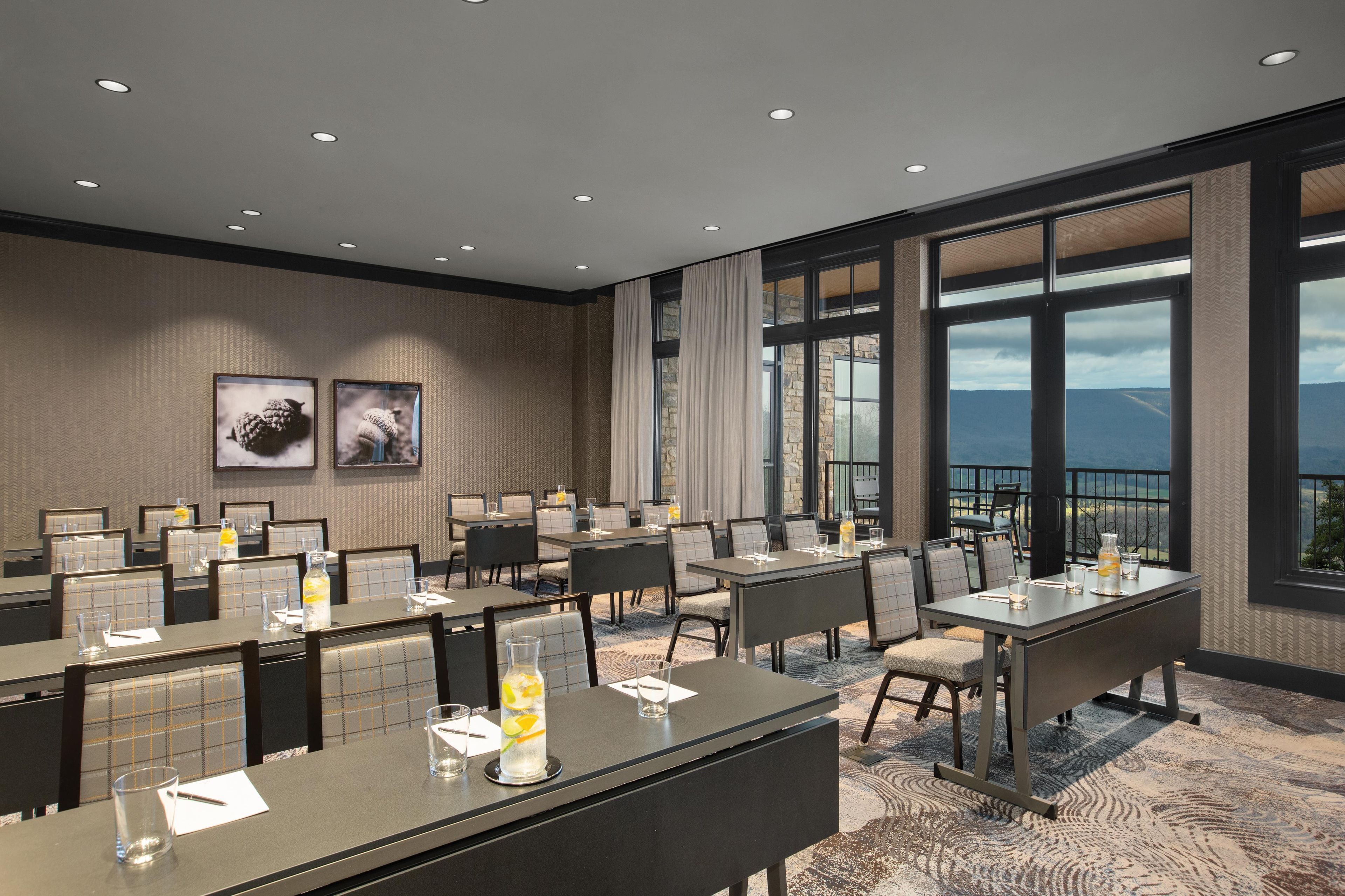 Une salle de conférence d’hôtel équipée de tables, de chaises et d’une grande fenêtre donnant sur un paysage.