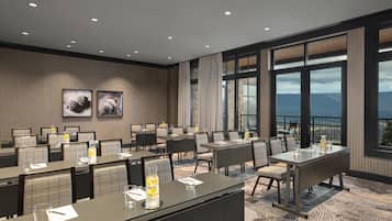A hotel conference room with tables, chairs, and a large window offering a view.