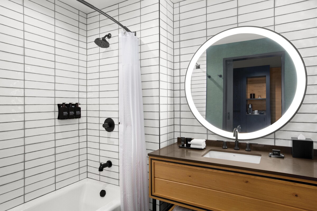 Une salle de bain moderne équipée d’une baignoire, d’une douche, d’un meuble-lavabo avec miroir et d’articles de toilette.