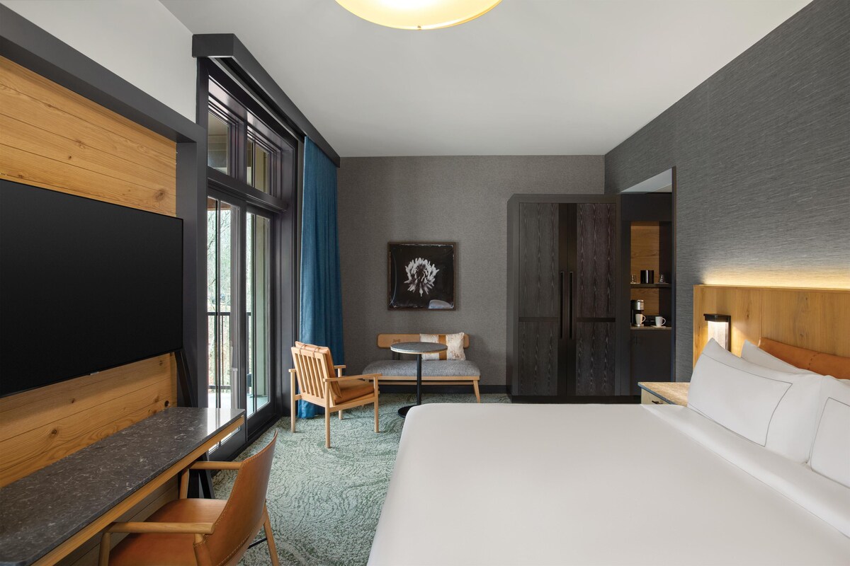 Une chambre d’hôtel moderne, dotée d’un grand lit, d’un bureau, d’une chaise, d’une petite table et d’une grande fenêtre.