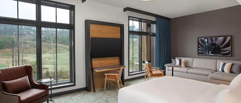 A hotel room with a large bed, a desk, a chair, a sofa, and a view of the outdoors.