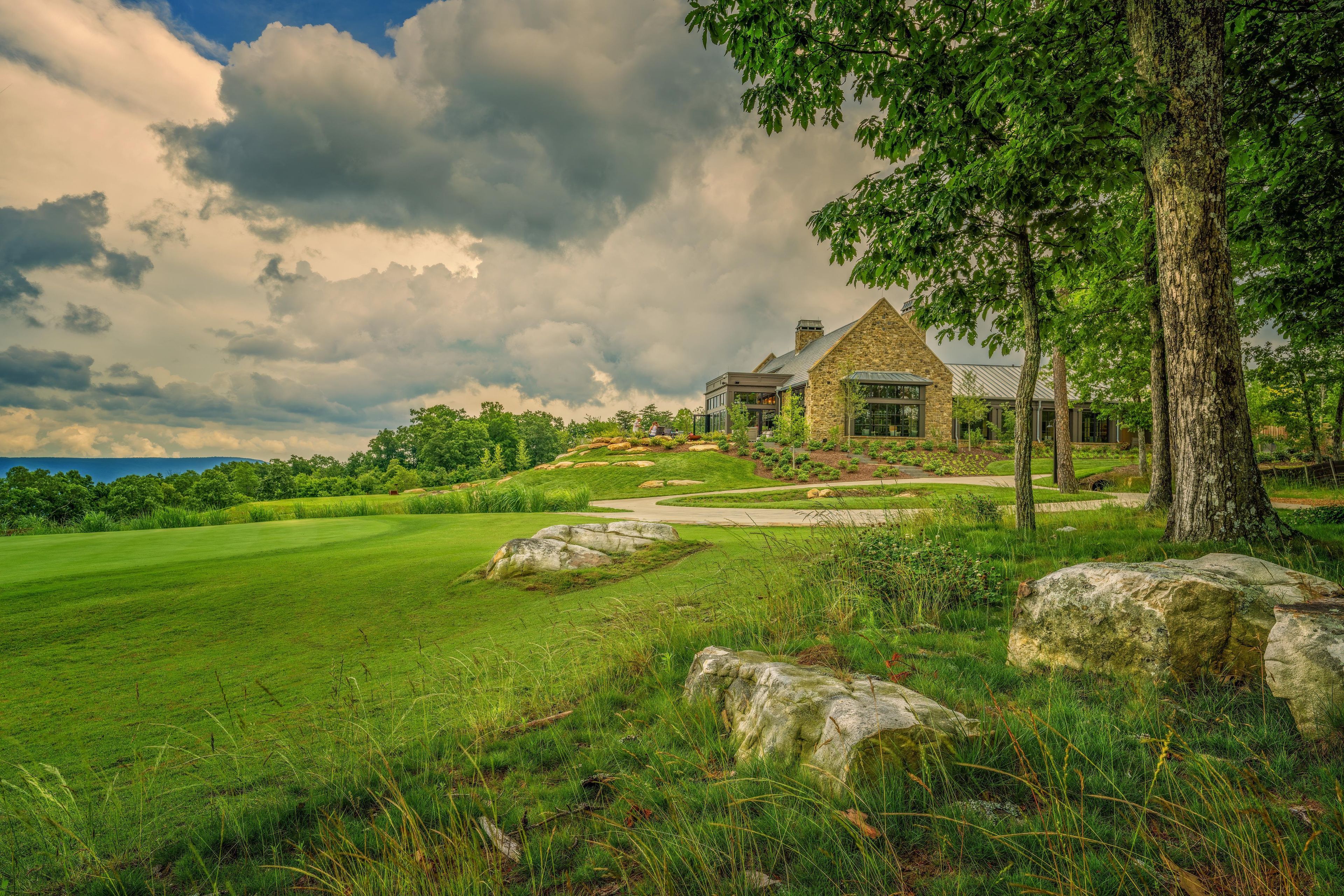 A stone house with a large window, surrounded by a lush green landscape and a golf course.