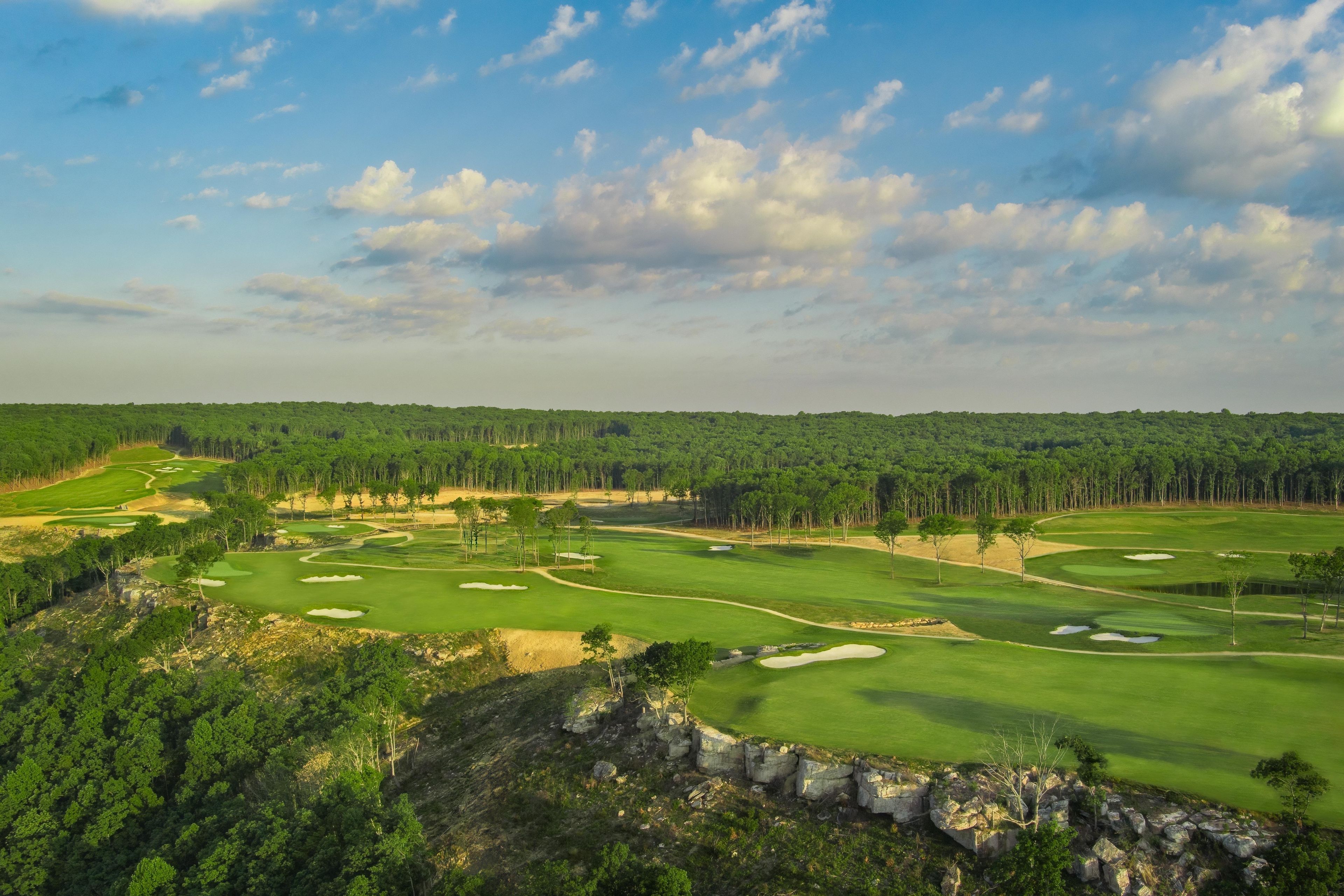 A golf course with a clear sky, trees, and a rocky outcrop.