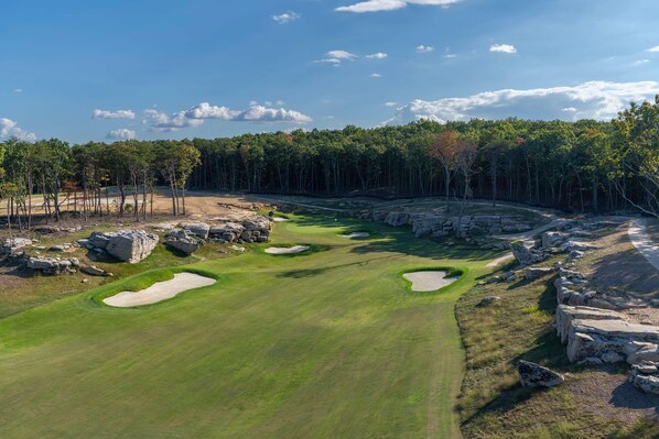 En golfbana med bunkrar, en klar himmel och en skog i bakgrunden.