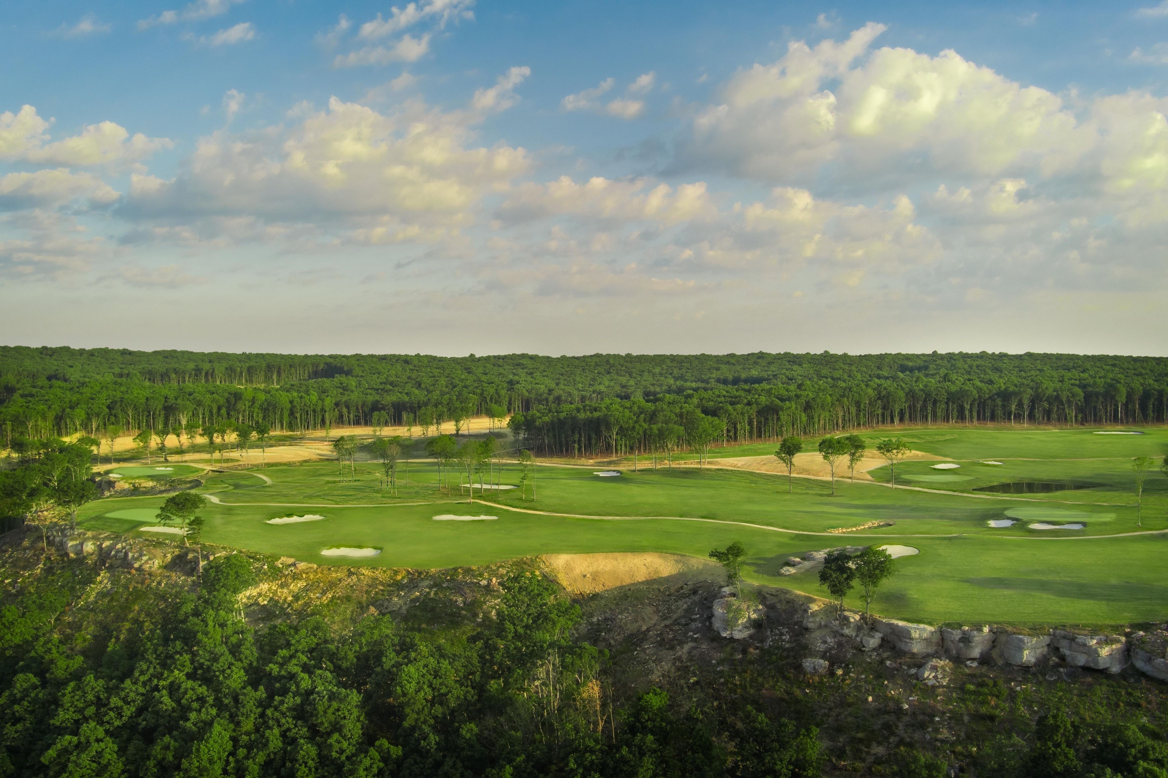 Un parcours de golf comportant plusieurs trous, des bunkers de sable et une forêt dense en arrière-plan.