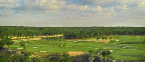 A golf course with multiple holes, sand bunkers, and a dense forest in the background.