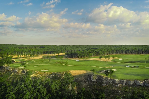 En golfbane med flere huller, sandbunker og en tæt skov i baggrunden.