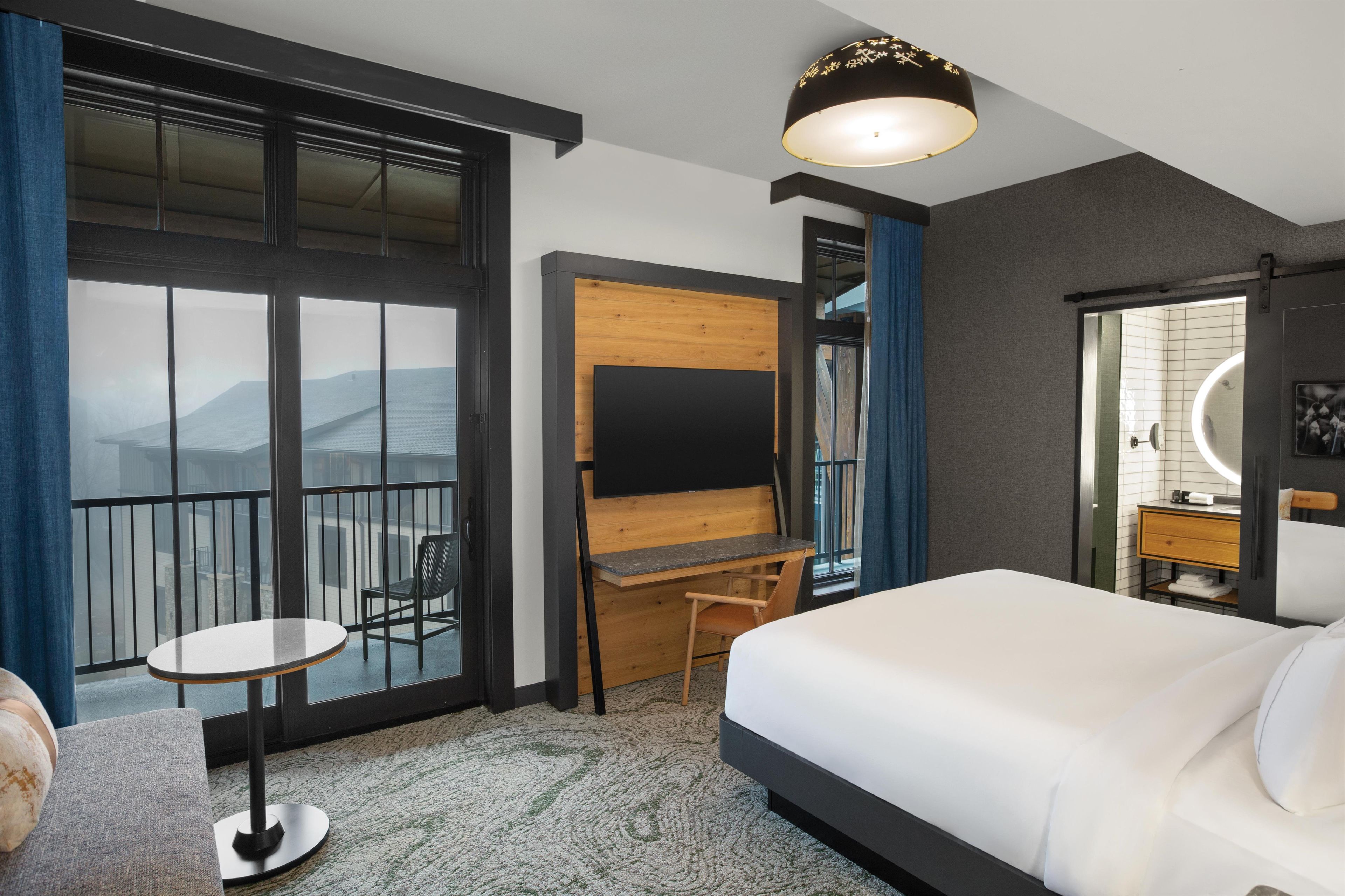 A hotel room with a bed, a desk, a chair, a TV, and a large window with a view.