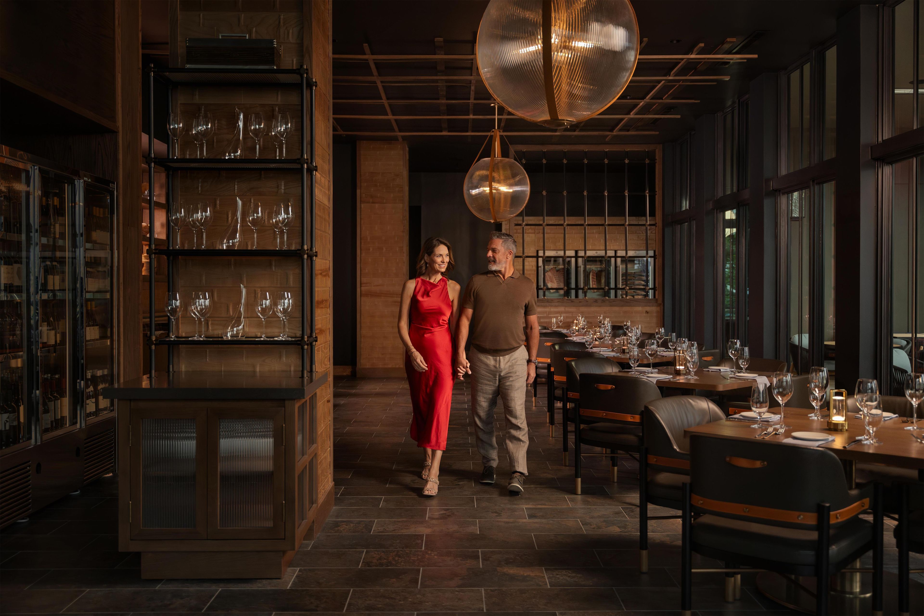L’intérieur d’un restaurant, avec un meuble à vin, des tables et un grand luminaire suspendu.