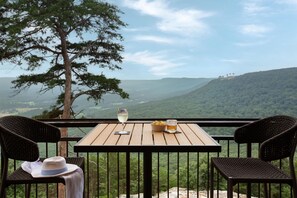 A wooden table with two wicker chairs, a hat, and a glass of wine on a balcony overlooking a mountainous landscape. - Cloudland Mclemore Resort Lookout Mountain Curio (Rising Fawn)