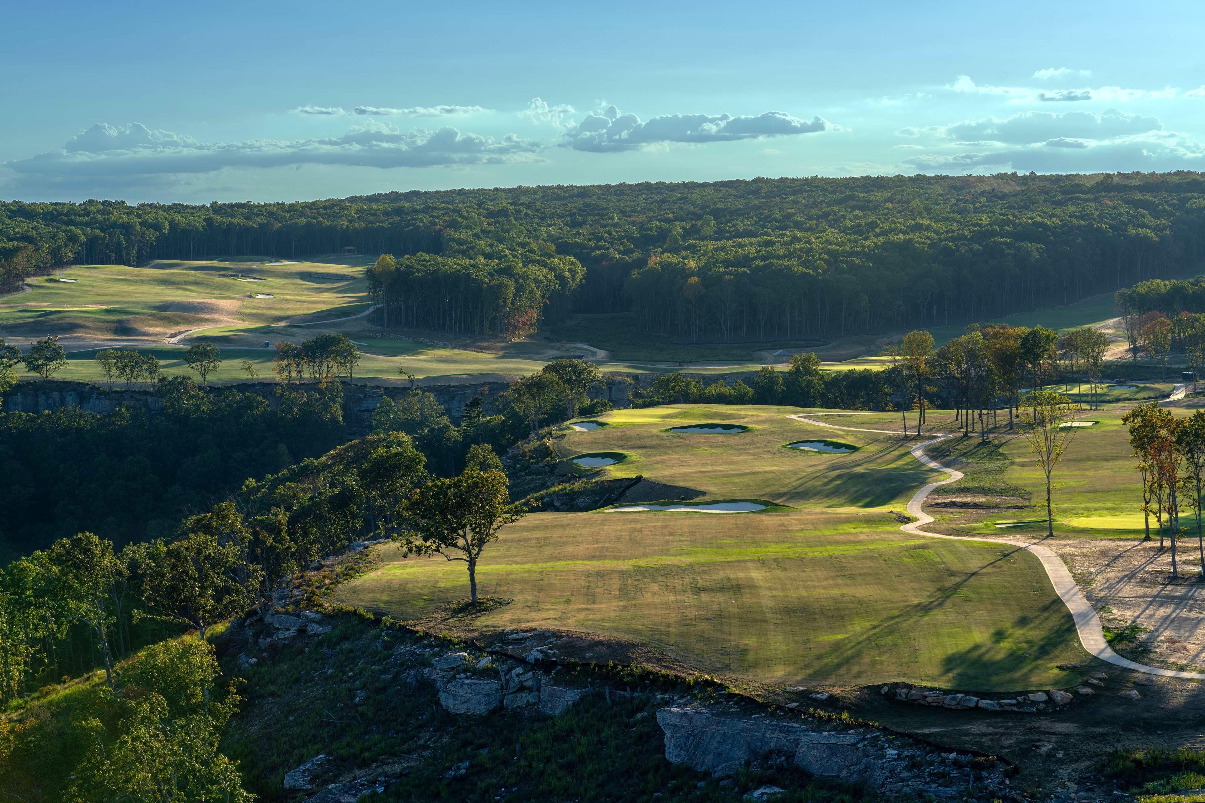 A golf course with multiple holes, trees, and a clear sky.
