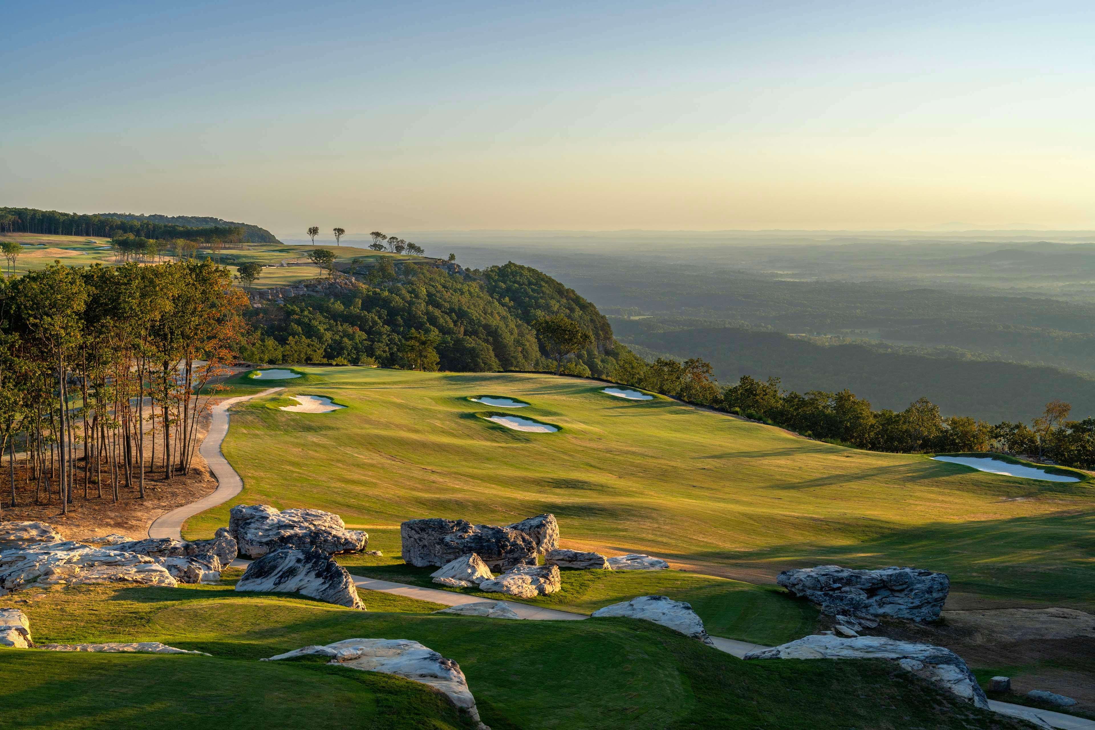 A golf course with bunkers, a winding path, and rocky outcrops.