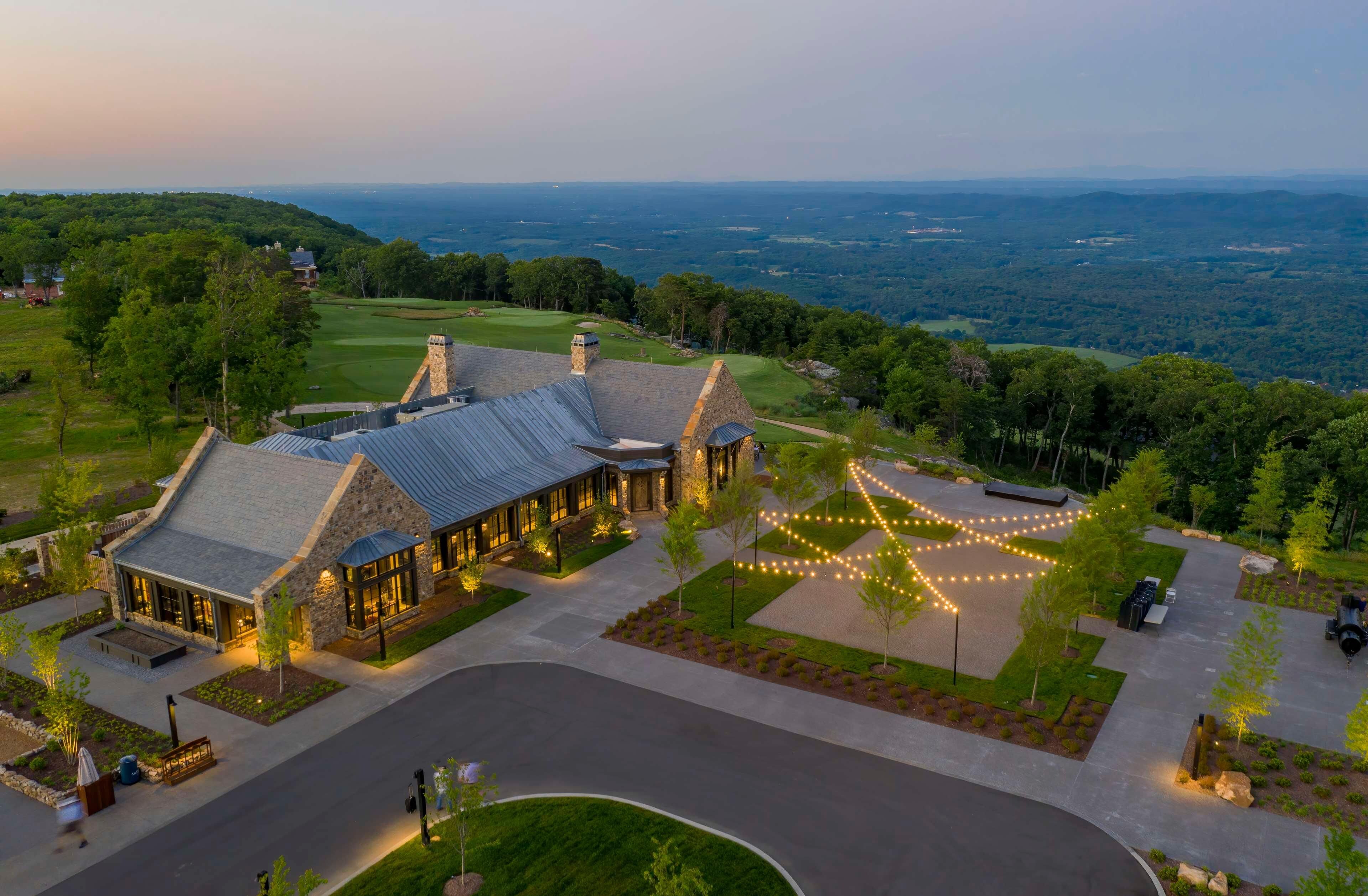 A large, stone building with a sloped roof, surrounded by a well-maintained lawn and a golf course in the background.