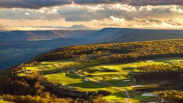 A golf course with multiple holes, a pond, and surrounding forested hills.