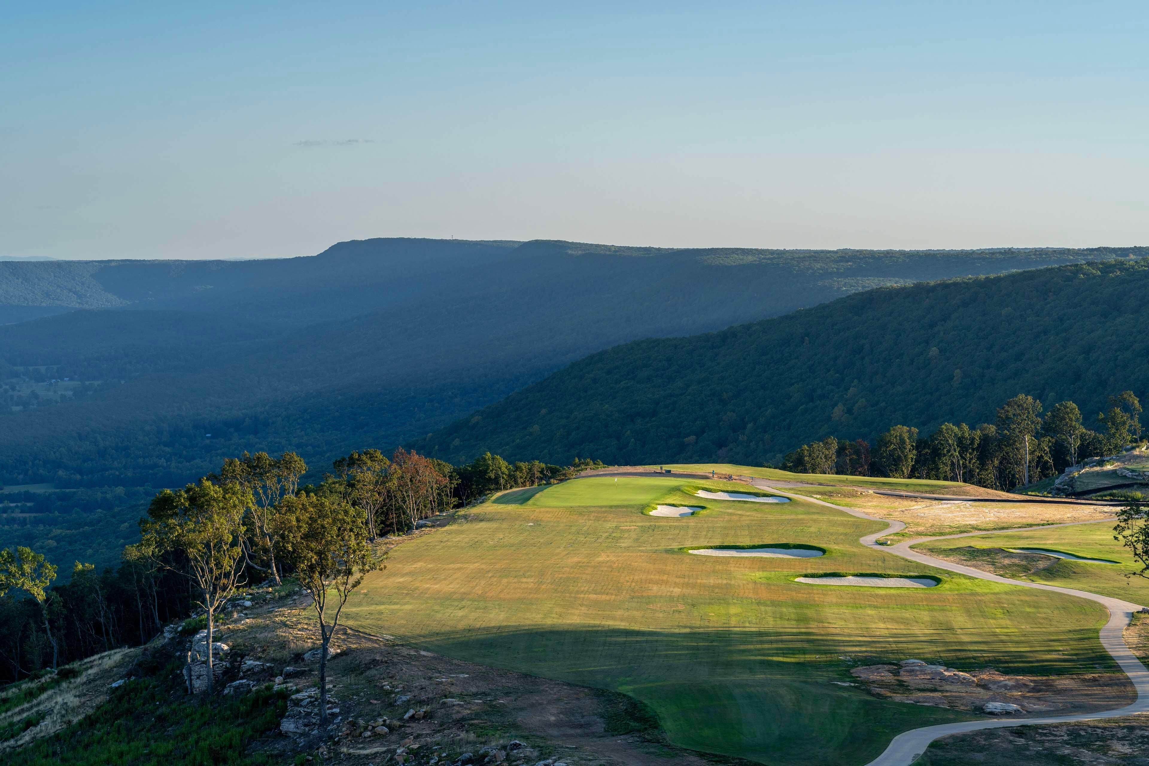 Un parcours de golf comportant plusieurs trous, entouré de collines douces et de forêts denses.